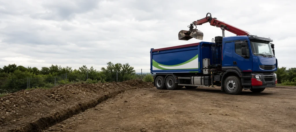 Blue grab lorry beside cleared utility trench spoil.
