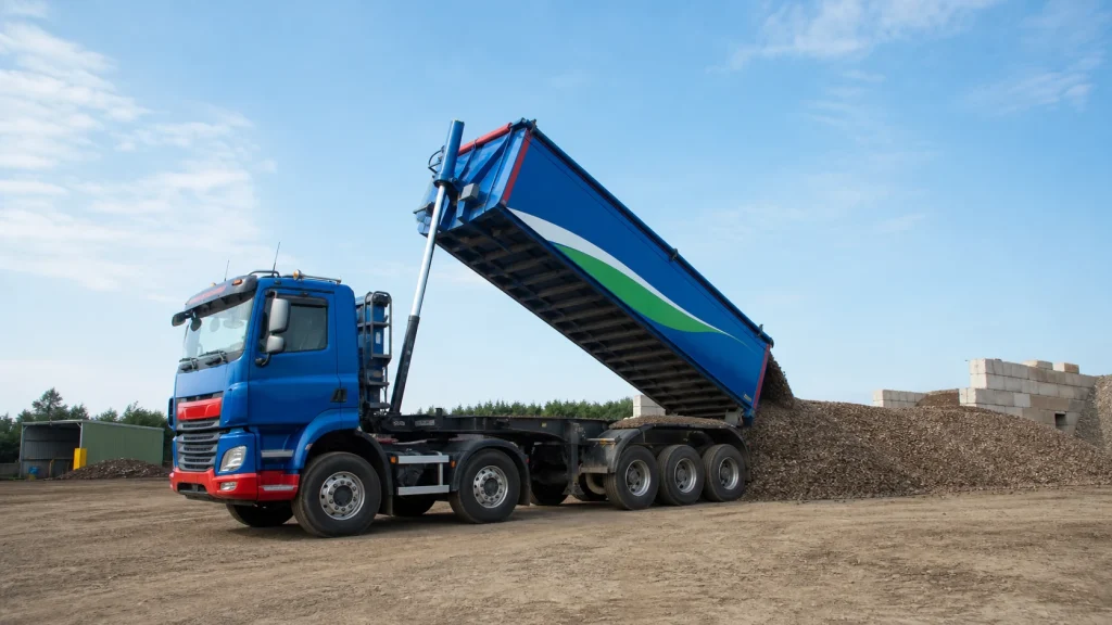 Blue tipper lorry tipping loose aggregate beside a material pile.